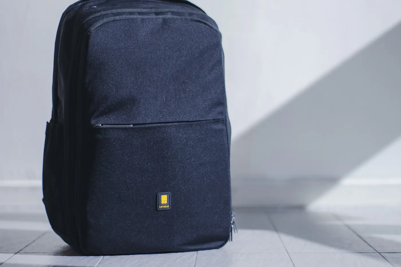 A navy laptop backpack photographed against a pale wall